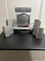 Panasonic SC-HT680 home theatre components including power amp, large woofer, 3 medium speakers, 2 small speakers arranged on a black surface.