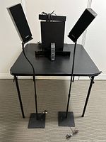 Sony Home Theatre System STR-K5370 components displayed including power unit console, two speakers on stands with wiring, small speaker, large woofer, and remote control on black table.