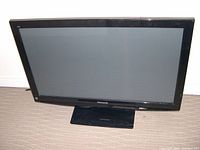Black Panasonic flat screen monitor with stand placed on carpeted floor.