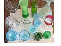 Top-down photo showing the vintage glass collectibles arranged around the boxed wooden Chinese Checkers board game with text visible on the board box.