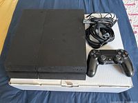 Sony PlayStation 4 console with one controller and cables placed on a box.