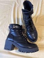 Pair of black women’s boots with chunky heels and ankle buckle strap, showing side profile and overall condition.