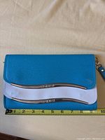 Women's blue and white leather wristlet purse laid flat with measuring tape showing about 8 inches in width, highlighting the front flap and metal bar detail.