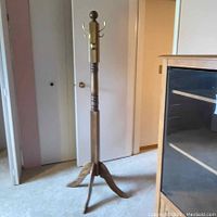 Full view of wooden coat rack standing in a room with white doors and beige carpet.