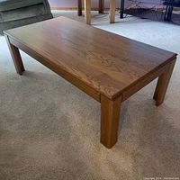 Wooden coffee table viewed from the side and angled, showing the table's sturdy legs and smooth grain wooden surface.