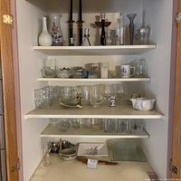 Five shelves displaying glassware, ceramics, candle holders, and decorative household items.
