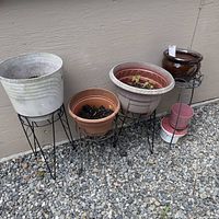 Wide angle view of five garden planters on metal risers arranged on gravel in front of a beige wall.