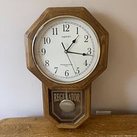 Front view of Ingraham octagonal wooden wall clock showing clock face, hands, and regulator display window.