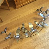 Full view of metal wall art with fifteen bird silhouettes mounted on curved wire frame, placed on hardwood floor.