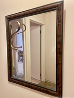 Full view of rectangular wall mirror hanging on a beige wall reflecting a doorway and part of a chair
