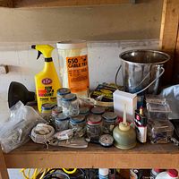 Photo of hardware supplies including STP protectant spray, large container of cable ties, jars with small metal parts, metal bucket, oil can, and assorted hooks and nails.