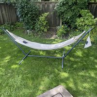 Full view of the white fabric hammock stretched on a black metal stand outdoors on grass, showing overall size and structure.