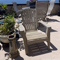 Taupe resin Adirondack chair in outdoor patio setting, showing front and back slats and armrests.