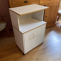 Front view of the rolling white kitchen cabinet showing the closed double door cabinet below and open shelf above on casters.