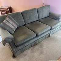 Front view of green fabric sofa with three cushions and one patterned throw pillow on arm.