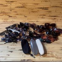 Overview of approximately 20 mixed sunglasses and three cases placed on a wooden surface.