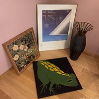 Photo showing all four items: tall wicker holder, Australian print, floral artwork, and frog painting arranged on a wooden floor in a corner with pink wall.