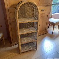 Full front view of the four-tier wicker display shelf standing on wood floor in front of wood cabinetry.
