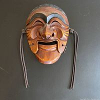 Front view of carved wooden mask with movable chin and attached cords.