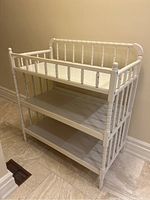 Front angle view of the white wooden baby changing table showing turned spindle design and three open shelves.