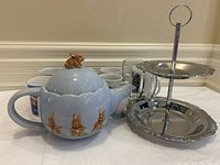 Photo of blue ceramic teapot with brown bunny figurine lid, 8 clear glass cups, and two-tier silver-tone serving dish