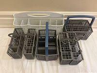 Front view of the eight dishwasher cutlery caddies lined up on the floor showing different sizes and handle styles.