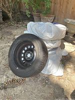 Four tires mounted on steel wheels, one leaning against wrapped stack