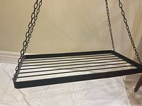 Black rectangular metal shelf suspended by three black chains, showing the hanging design and chain detail.