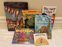 Six dinosaur themed children's books displayed upright and flat on a surface, showing cover art and titles.