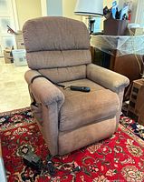 Front view of brown recliner with remote control on seat and power adapter on floor