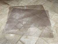 Two clear rectangular office chair mats placed overlapping on a tiled beige floor; mats are slightly warped from rolling storage.