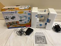 Dressmaker II sewing machine in original packaging with foot pedal, power adapter, and instruction manual.