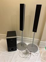 Photo showing two Sony satellite speakers on silver stands and one Sony subwoofer on floor with speaker wires.