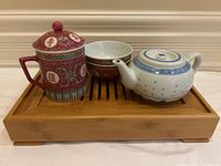Tea set on bamboo tray showing ornate cup with lid, two matching bowls, and small teapot