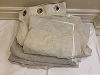 Two folded beige curtain panels with metal grommets, showing overall condition and size