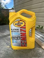 Front view of unopened yellow 5L Pennzoil Platinum High Mileage 5W-30 full synthetic motor oil container with handle and label visible outdoors.