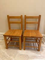 Front-facing photo of two small wooden kids chairs side by side with visible scratches on seat and backrest