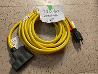 Full view of yellow extension cord coiled neatly on floor with handwritten label '220 Volt Extension Cord'