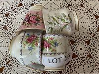 Four bone china tea cups laid on their sides showing floral patterns and gold trim.