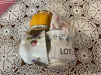 Four stacked bone china cups showing floral and yellow designs.