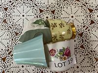 Four bone china cups and matching saucers stacked showing variety of colors and floral patterns on a crocheted tablecloth.