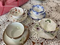 Four bone china cups with matching saucers arranged on crochet cloth displaying different floral patterns and rim designs.