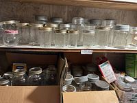 Shelf with assorted glass canning jars and lids, some in boxes below.