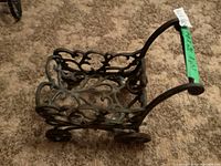 Side angle of cast iron decorative wagon planter showing ornate scroll and floral designs on sides and wheels.