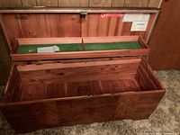 Open wooden Lane cedar chest showing interior wooden panels and green felt-lined compartment tray with metal lock clasp; exterior has wood grain finish.