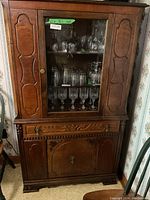 Full view of the wooden china cabinet showing glass doors filled with glassware and lower storage compartments with carved panel doors and brass hardware.
