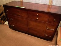 Full front view of wooden dresser with multiple drawers and brass-colored hardware, showing dark finish and dovetail joinery.