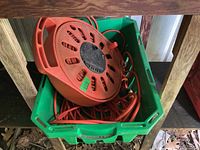 Green plastic bin holding a round orange extension cord reel and a loose orange extension cord inside.