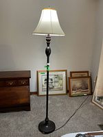 Full view of the floor lamp showing its height, base, and lampshade in a room setting with framed pictures and furniture around it.