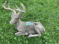 Side view of reclining buck deer statue on grass showing antlers and body detail